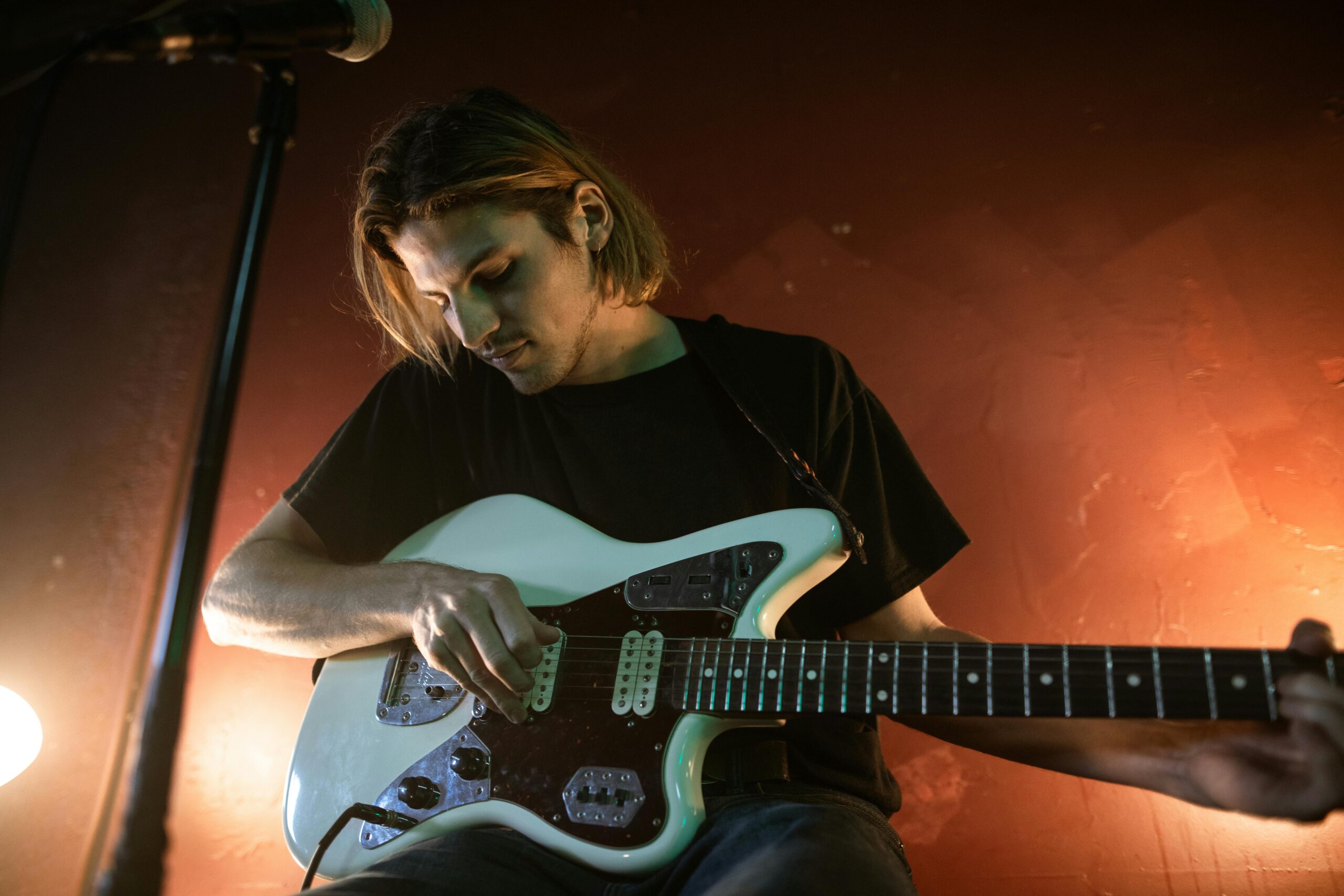 Oferta Male musician playing electric guitar at a bar with warm lighting.