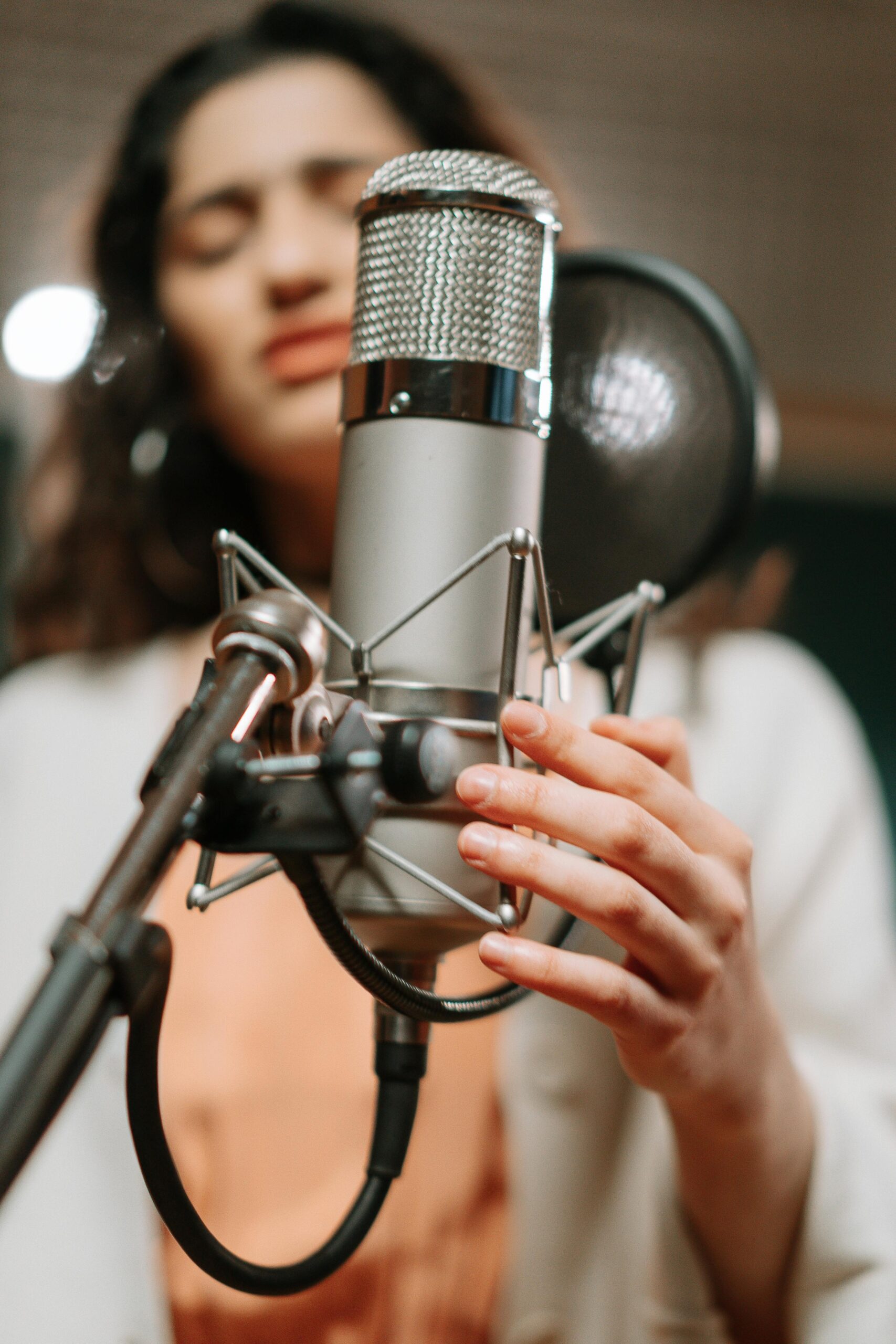 Oferta A woman singing passionately into a condenser microphone in a modern music studio.